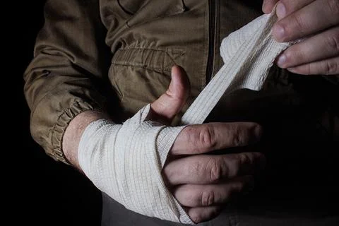 Man in tactical jacket taking care of wounded hand with medical care bandage. Stock Photos
