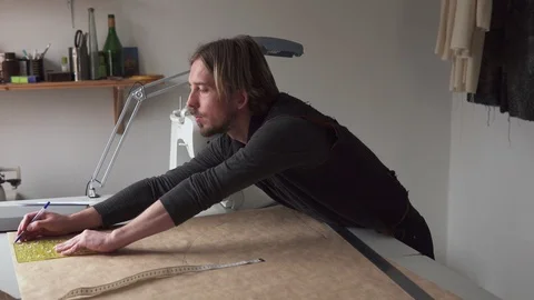 Man tailor draws clothing pattern while working in workshop Stock Footage 100617411