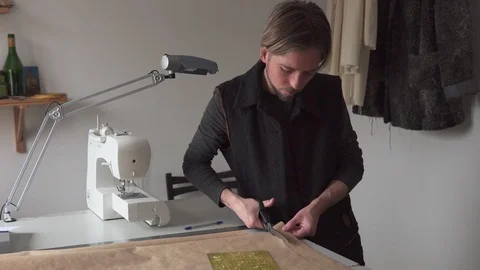 Man tailor with scissors cuts paper clothing pattern in workshop Stock Footage 100617590