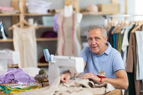 Man tailor sews on sewing machine in workshop Photos
