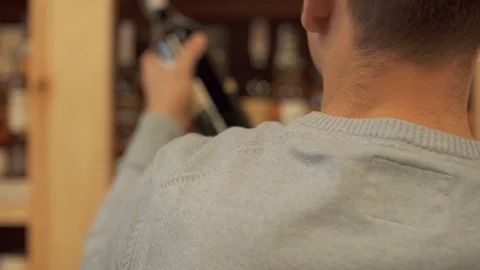 Man takes and puts back wine bottle closeup Customer is choosing drink in Stock Footage 99385427
