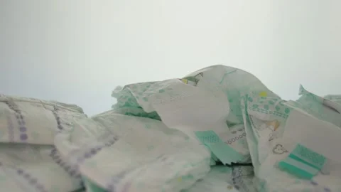 A man takes a baby diaper from a stack of scattered baby diapers on a white Video stock 253470493