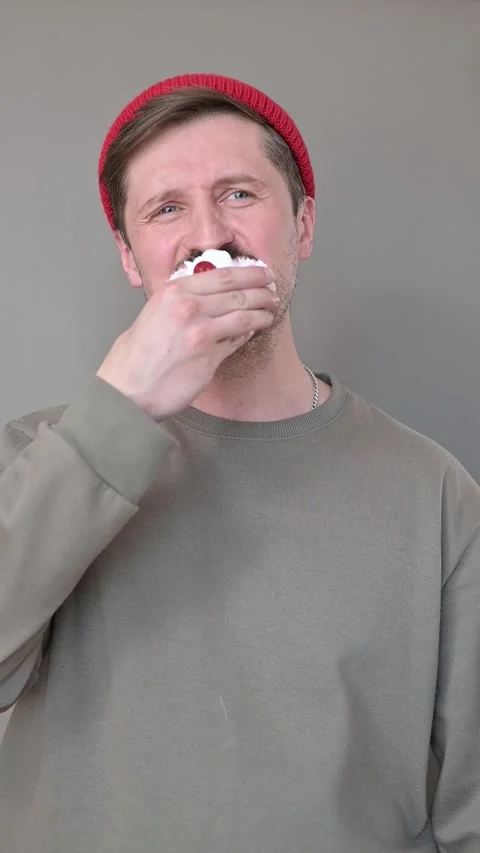 A man takes a bite of dessert while wearing a red beanie and gray sweater. This Stockbeeldmateriaal 337556134
