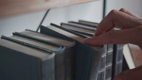 A man takes a book from a row of books on a bookshelf. Old books in leather bind Stock-Footage 233028448