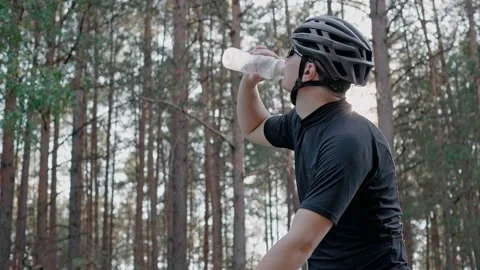 Man takes bottle and drinks water after riding on bike in a pine sunny forest Vídeo Stock 166173871