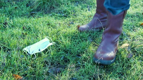 Man takes off face mask, throws it on ground and crushes it with foot in park Stock Footage 149310198