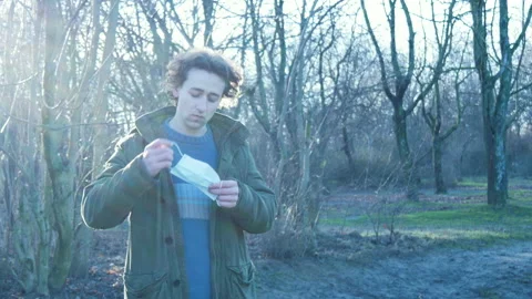 Man takes off face mask, throws it on ground and crushes it with foot in park Stock Footage 149317507