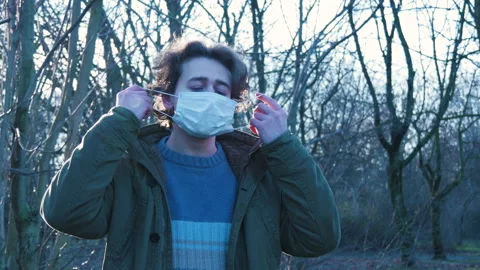 Man takes off face mask, throws it on ground and crushes it with foot in park Stock Footage 149319802