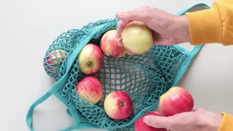 Man takes fresh red apples out from reusable grocery bag with fruits on a table Video stock 219917474