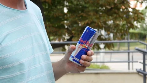 Man takes in Hand a Can of Red Bull Energy Drink on a Street Stock Footage 113797152