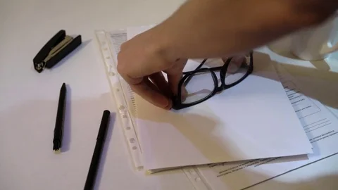 The man takes his glasses from the table. on a white table lie papers and pens. 库存影片 83467401
