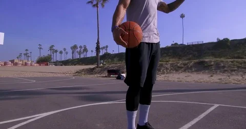 A man takes a jump shot while playing one-on-one basketball hoops on a beach cou Stock Footage