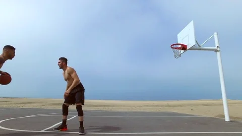 A man takes a jump shot while playing one-on-one basketball hoops on a beach cou Stock Footage