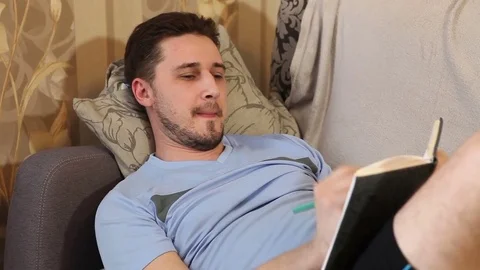Man takes notes in a notebook lying on the couch Stock Footage 72581485