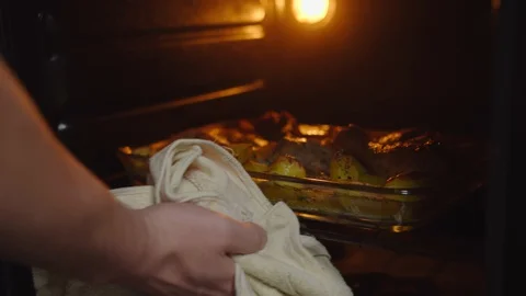 Man takes out a baking sheet with baked food chicken legs and potatoes Stock Footage 130062602
