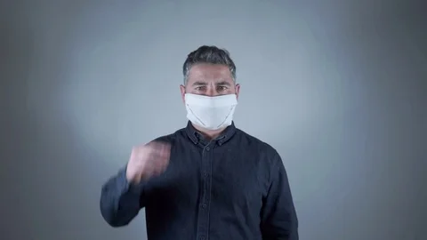 Man takes off protective mask looking towards camera on gray background Stock Footage 129420723