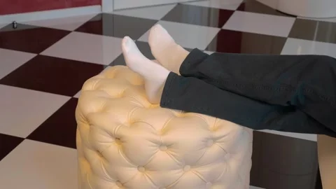 A man takes the remote control from a white leather round ottoman and sits down Stock Footage 297744214