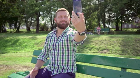 Man takes selfie on bench in park. Steadicam. Vídeos de archivo 67235448