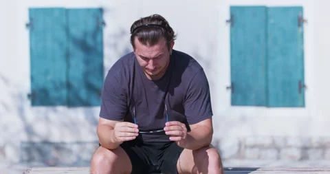 Man takes off sunglasses while sitting on bench by building Stock Footage 257638418