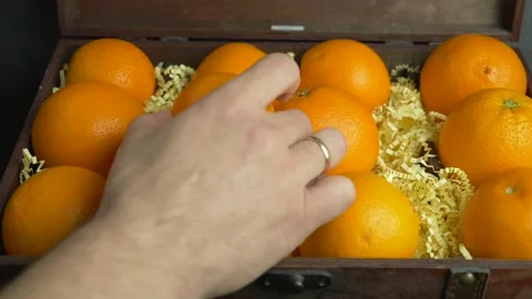 The man takes the two oranges that lie in the chest. Stockbeeldmateriaal 231105986