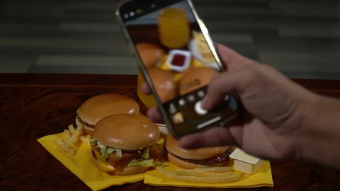 A man takes a vertical photo of a fast food burger on a table using a smartphone Video stock 260395953