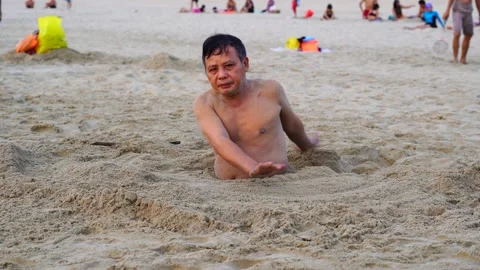 Man taking a bath of beach sand for therapy near sea water in morning, Vietnam Stock Footage 134018214