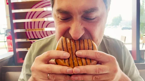 A man is taking a big bite of a grilled burger inside a fast-food restaurant. He Stock-Footage 310582140