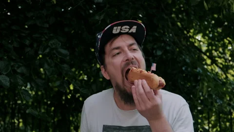 Man taking a big bite of hot dog outdoors Video stock 133616551