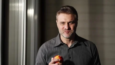 Man Taking a Bite of an Apple in front of a window at home. Concept of healthy Stock Footage 262645739