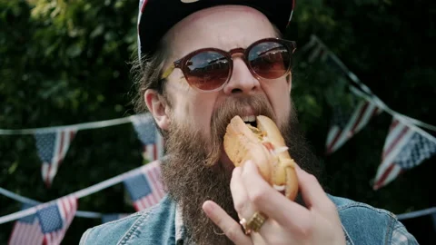 Man taking a bite of hot dog at 4th of July outdoors party Video stock 133616083