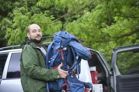 Man taking his backpack out of his car at the start of a journey into nature. Stock Photos