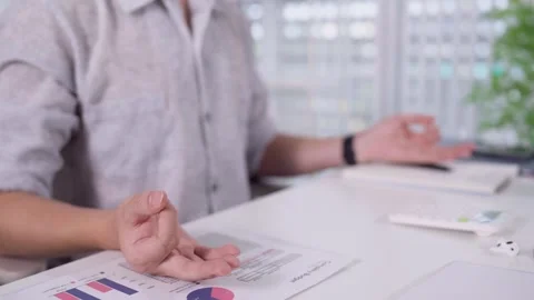 Man taking mindful break with meditation gesture beside financial charts at.. Stock Footage 345156774