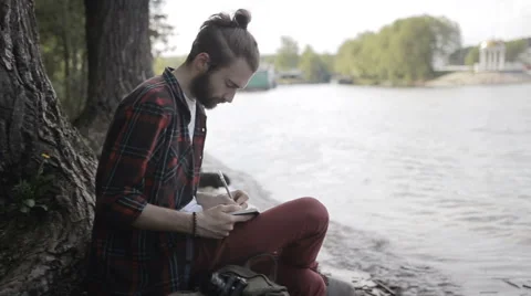 Man taking notes in a notebook sitting on the shore 動画素材 65221211