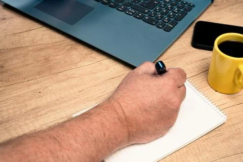 Man taking notes in a notepad next to his laptop while working at home or off Stock Photos