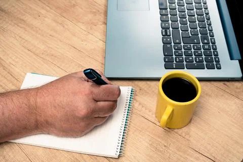 Man taking notes in a notepad next to his laptop while working at home or off Stock Photos