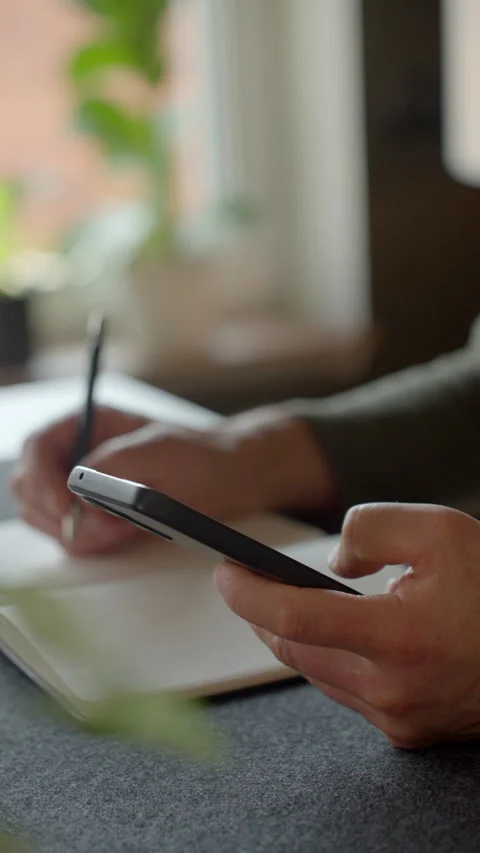 Man taking notes from phone sitting at home desk Stock Footage 333493574