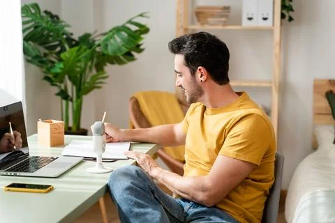 Man taking notes while watching online classes. Stock Photos