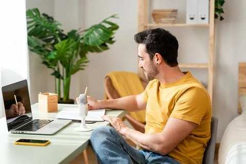 Man taking notes while watching online classes. Stock Photos