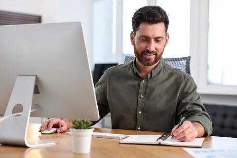 Man taking notes while working on computer at table in office 스톡 사진