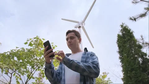 Man taking notes on wind turbine performance, standing in a park with a windmill Stock Footage 300250633