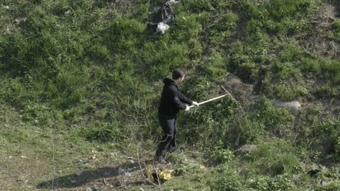 Man taking part in volunteering cleanup and picking garbage with rake Stock Footage 90051251