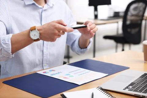 Man taking photo of document using scanning app on smartphone at desk in of.. Stock Photos