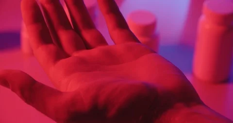 Man taking pills out of can in neon light, representing modern drug and medicine Stock Footage 119048464