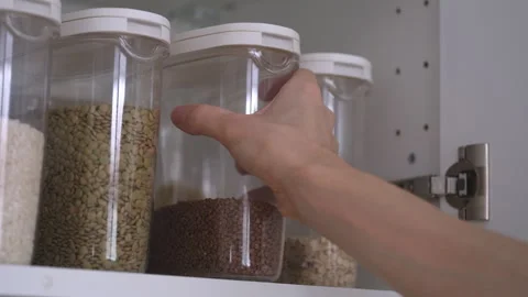 A man taking a plastic container of buckwheat out of a kitchen cabinet. Stock Footage 297632549