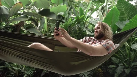 Man taking selfie on smartphone while sitting on hammock, exotic background Stock Footage 84841150