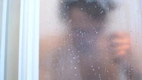 Man taking a shower standing under flowing water in shower cabin behind Stock Footage 102542298