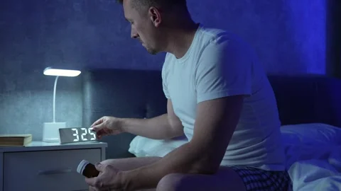 Man taking sleeping pills in bedroom at night. Insomnia and sleep problems .. Stock Footage 289562014