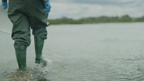 Man taking soil samples in water waders and boots with female assistant - mid Stock Footage 106425496
