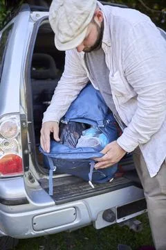 Man taking something out of his backpack that is in the trunk of his car. Stock Photos