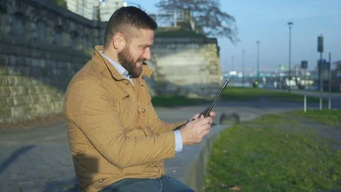 Man taking video call by tablet computer, sitting on wall at boulevard, river Vídeo Stock 72775467
